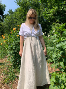 Woman wears a flowy linen maxi dress and white linen wrap top in a flower garden