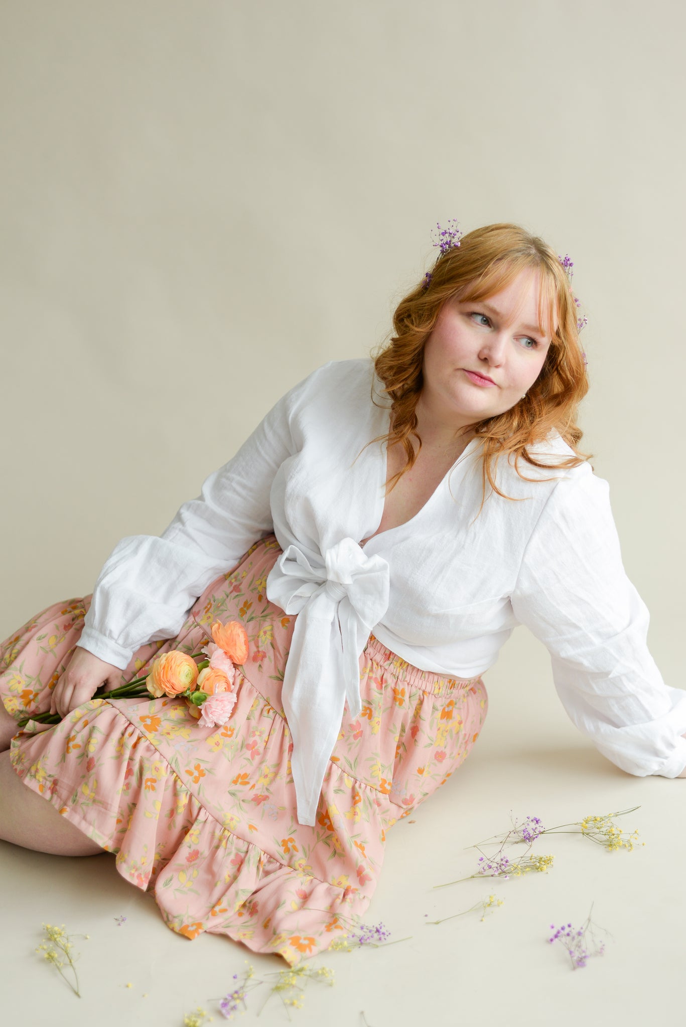 model sitting on the floor wearing a white wrap top and a floral skirt