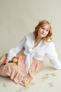 model sitting on the floor wearing a white wrap top and a floral skirt
