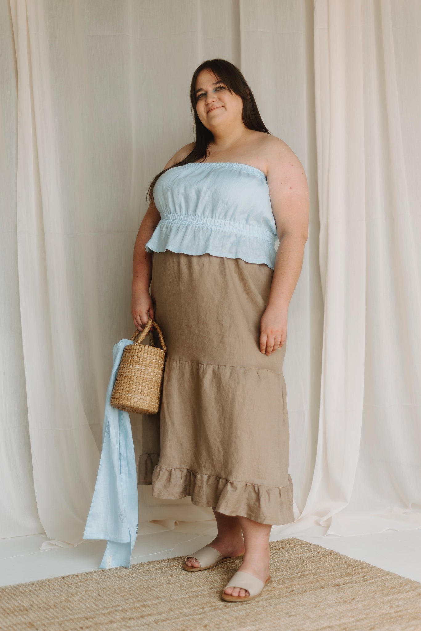 blue tube top worn with tiered beige skirt and a straw purse with a blue scarf on it