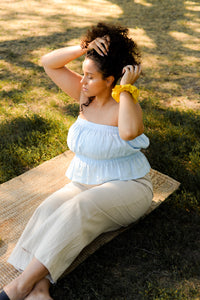 woman sitting in the grass wearing a pale blue strapless top and beige pants