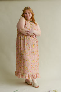 plus size female model smiling while wearing a soft pink floral maxi dress