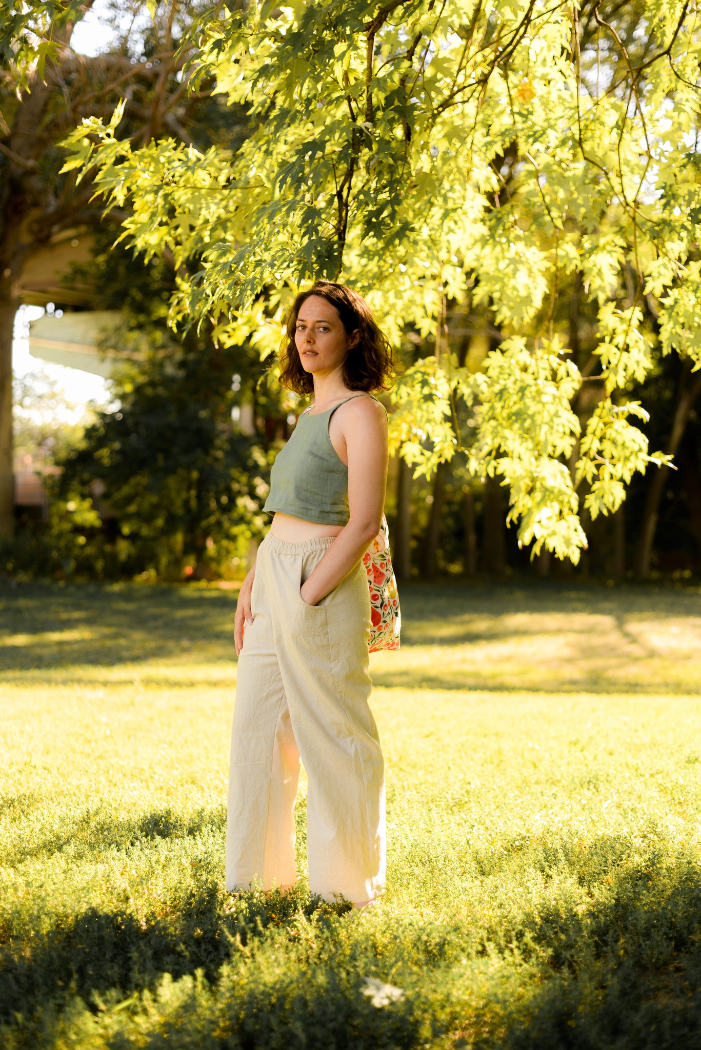 woman standing in a park wearing wide leg beige linen pants and a green crop tank top
